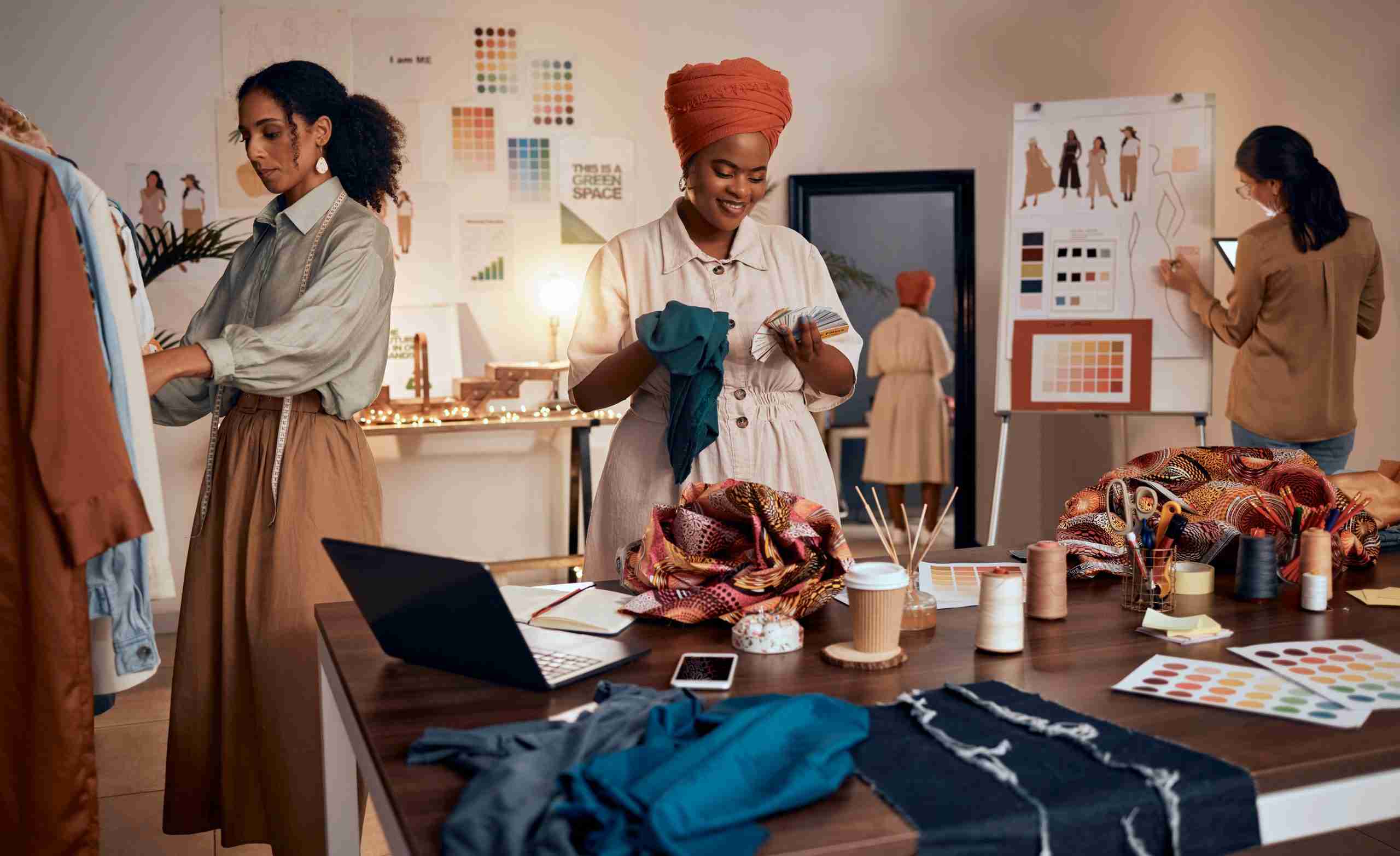 A fashion design studio where three designers, united by the integration advantage, work seamlessly: one examines fabric at a desk, another evaluates garments on a clothes rack, while the third sketches near a mood board. Together, they build their business into a cohesive masterpiece.